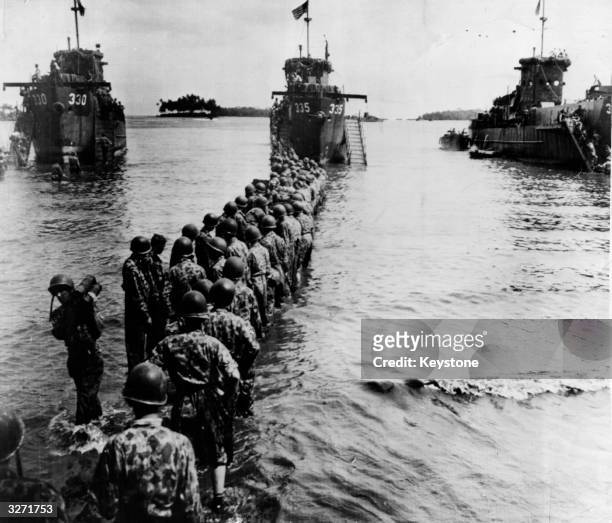 United States Marines, in camouflage, form a line in the surf to pass munitions from three landing craft carriers onto the shore during the seizure...