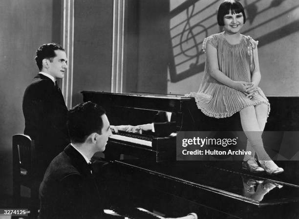 Baby Rose Marie, the child actress sits on one piano, resting her feet on another while two gentlemen play in a scene from the film 'International...