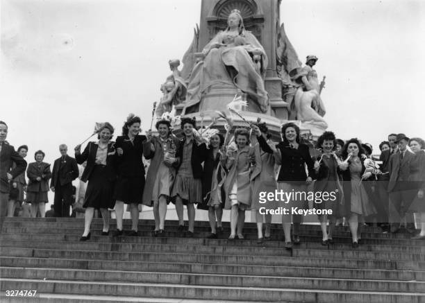 Group of London girls waving flags in front of the statue of Queen Victoria outside Buckingham Palace on VE Day, 8th May 1945.