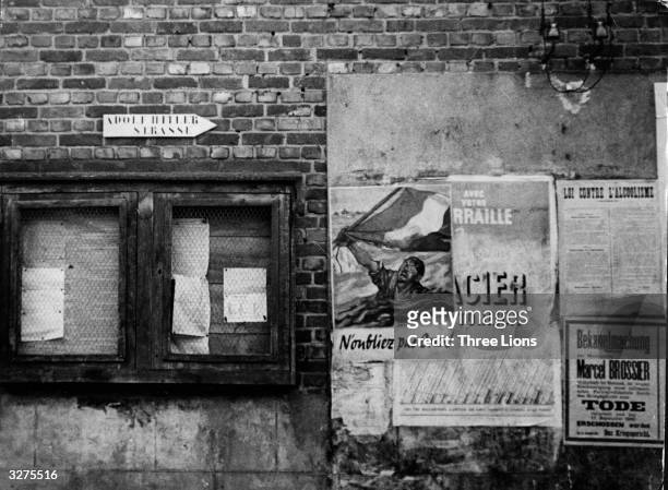 Adolf Hitler street in French territory occupied by the Nazis with a poster of a French soldier waving a French tricolor as he goes down with his...