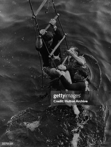 Three men being rescued from the sea after having to abandon ship as they were evacuated from the beaches at Dunkirk. They cling to a ladder let down...