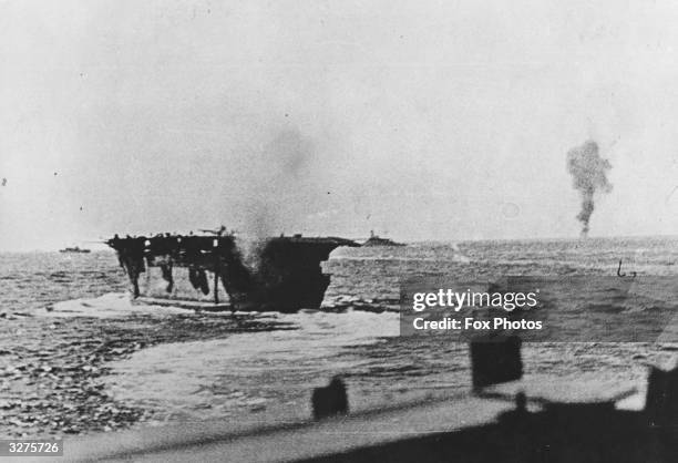 The aircraft carrier HMS Argus in the foreground, smoke rising from an enemy plane in the background, shot down during an attack on the Malta bound...