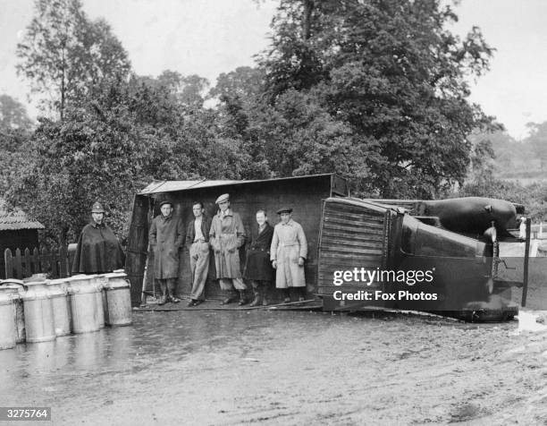 Passers-by use an overturned lorry as a shelter during a sudden shower of rain near Navestock, Romford, Essex. The lorry overturned on a sharp bend,...