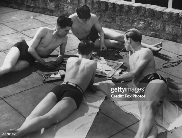 Group of sunbathers, having a smoke and playing a game of monopoly at an open air pool.