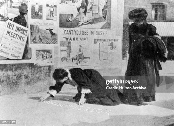 Suffragettes Annie Kenney and Mary Gawthorne painting a pavement with a slogan, 'Votes For Women', during the Hexham by-election.