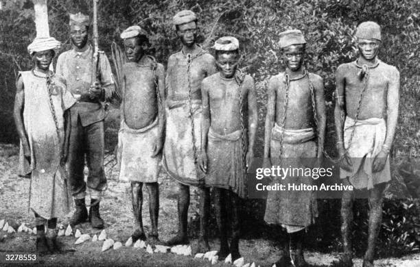 Enslaved men in chains, guarded by a native Askari, or soldier,circa 1896.