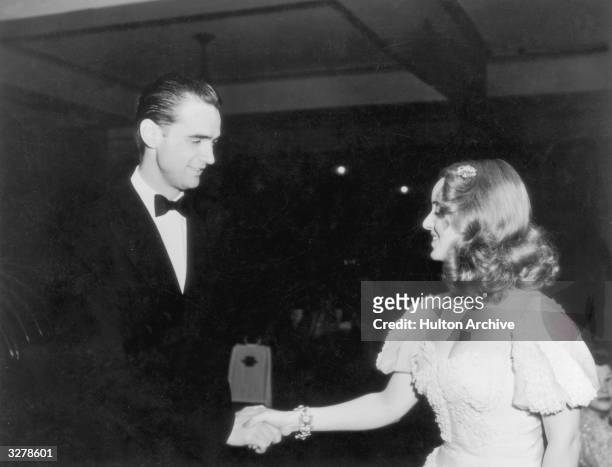 American industrialist, aviator, and film producer Howard Hughes shakes hands with American actress Bette Davis at the Tailwaggers party, thrown by...