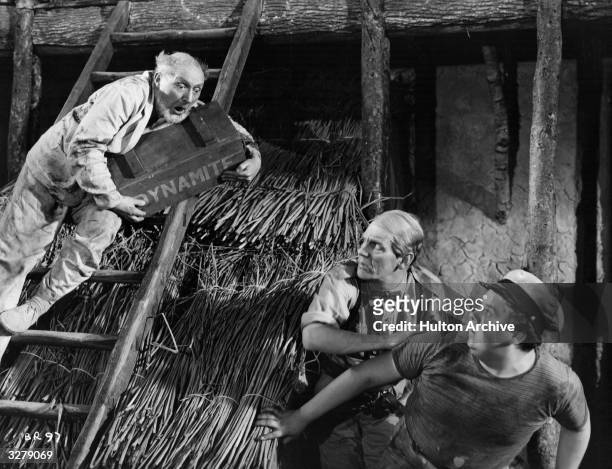 British actor Moore Marriott is halfway up a ladder, about to drop a large case of dynamite onto his colleagues, Graham Moffatt and Will Hay , in a...