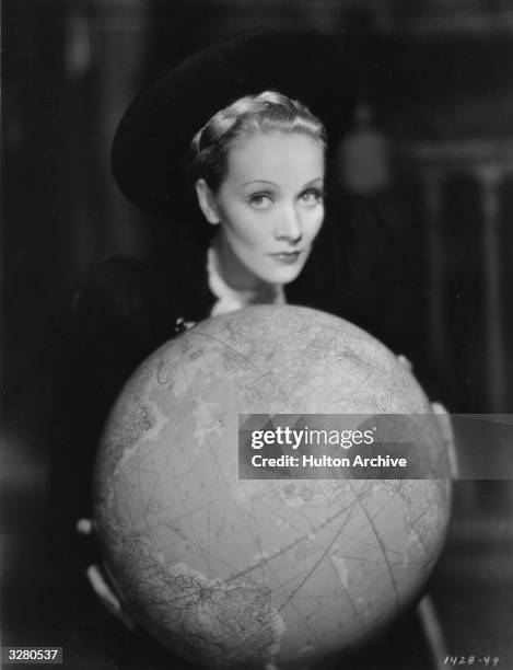 German-born actress and singer Marlene Dietrich holding a globe during the filming of 'Song Of Songs', directed by Rouben Mamoulian for Paramount.