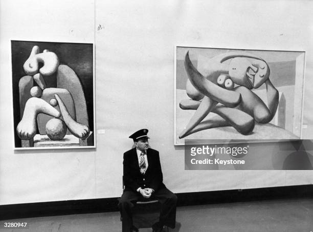 An attendant at the Grand Palais des Champs-Elysees sits patiently between two of Picasso's paintings on exhibition there. 'The Woman In A Red Chair'...