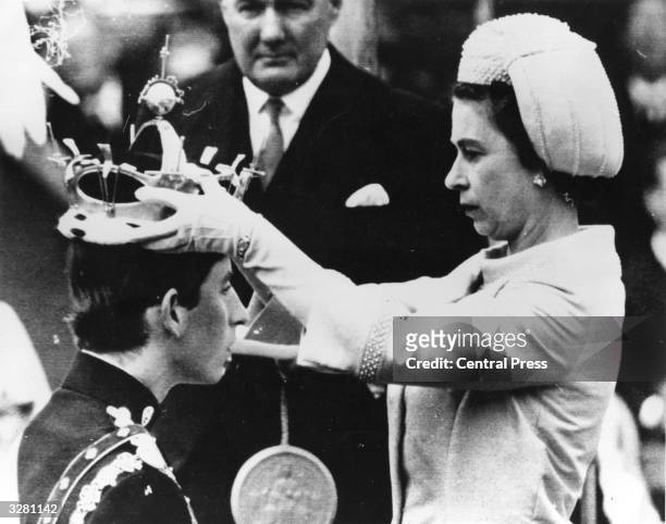 The Queen placing the coronet of The Prince of Wales on Charles, Prince of Wales' head during his investiture ceremony whilst an official holds the...
