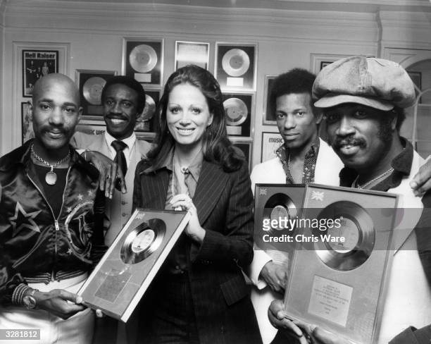 Author Jackie Collins presenting pop group Hot Chocolate with silver discs for the sales of their single 'Emma', number two in the British charts....