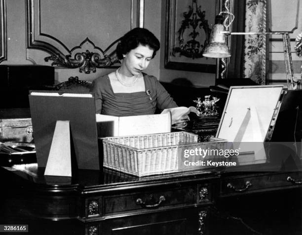 Queen Elizabeth II reading the contents of her official boxes, containg details of her country's political affairs at her desk in Buckingham Palace,...