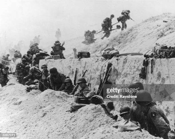 American troops advance over the crest of a concrete sea wall after the successful landings on Utah Beach in Normandy, France, whilst comrades...
