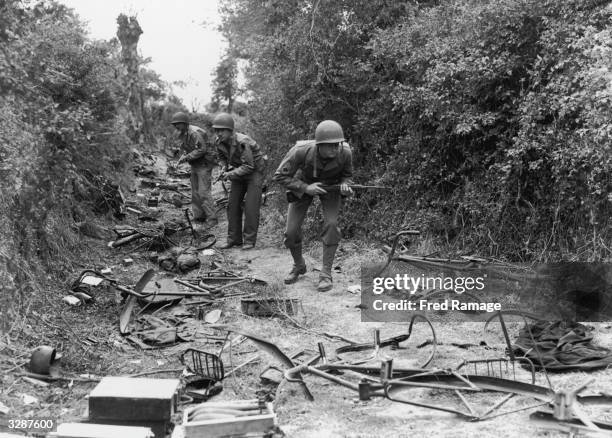 American troops advancing through a wood near Valognes, on the Cherbourg front. The track is littered with parts of bicyles and ironmongery.