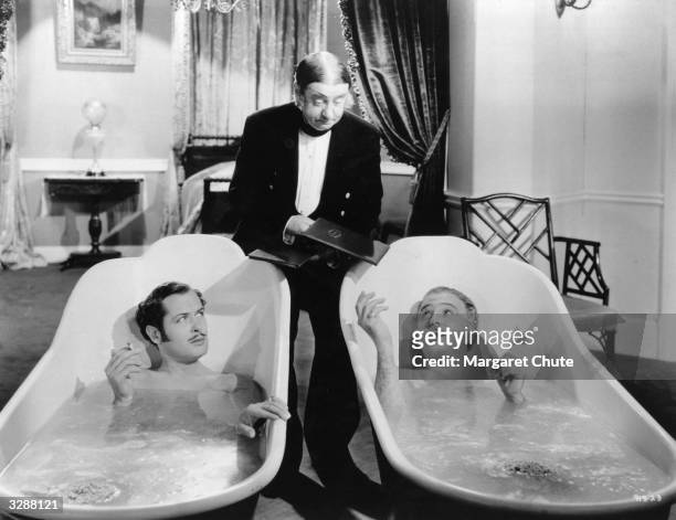 Robert Montgomery and Frank Morgan are handed menus by their butler whilst reclining in hip baths, in a scene from the film 'Suicide Club', directed...