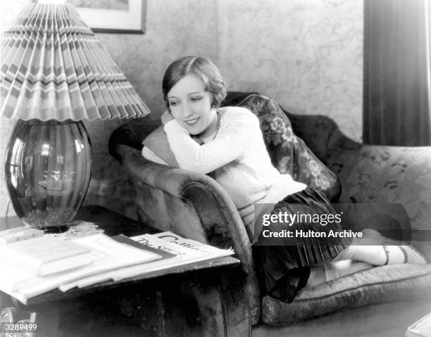 Bessie Love , the Hollywood actress who appeared in 'Dress Parade' curls up in a chair in her Hollywood home.