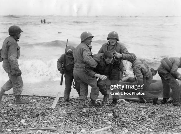 American troops helping their injured friends from a dinghy after the landing ship they were on was hit by enemy fire during the Allied invasion of...