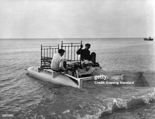 Two men sit on board a floating bedstead in the sea near Dover.
