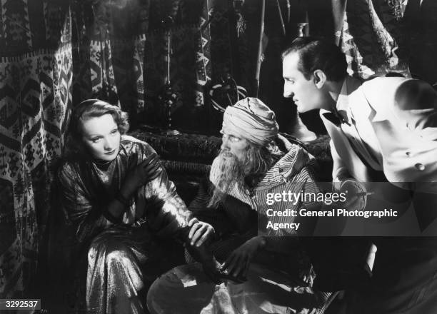 Marlene Dietrich and Basil Rathbone consult holy man John Carradine in the David O Selznick film 'The Garden Of Allah', directed by Richard...