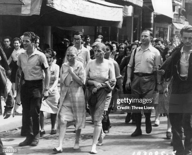 Two women, partially stripped, their heads shaved and with swastikas painted on their faces, are marched barefoot down the streets of Paris, to shame...