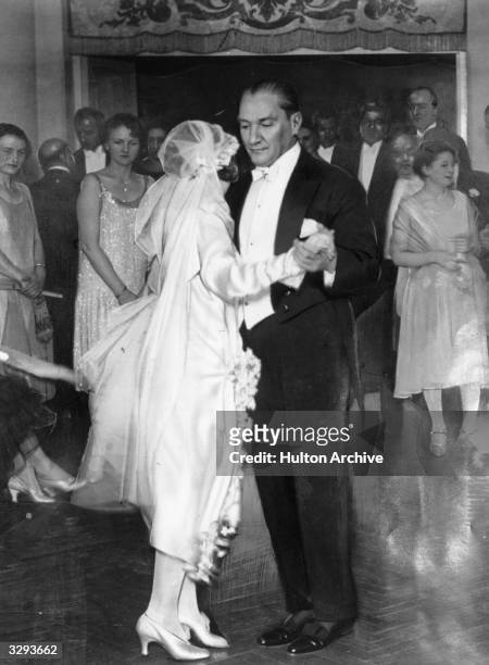 Guests clustered in a doorway watch as Mustafa Kemal Ataturk, President of the Turkish Republic, dances with his adopted daughter at her wedding. The...