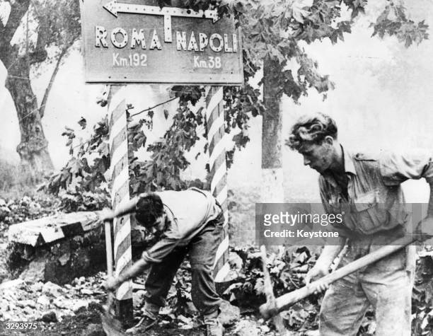 Two sappers of the British engineers, do a bit of pick and shovel work on the road to Rome by way of making a contribution to the smoother advance of...