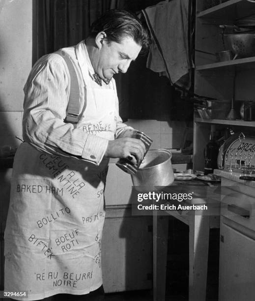 British conductor and cellist Sir John Barbirolli cooking in his Manchester flat. The apron covered with the names of his favorite dishes is a gift...