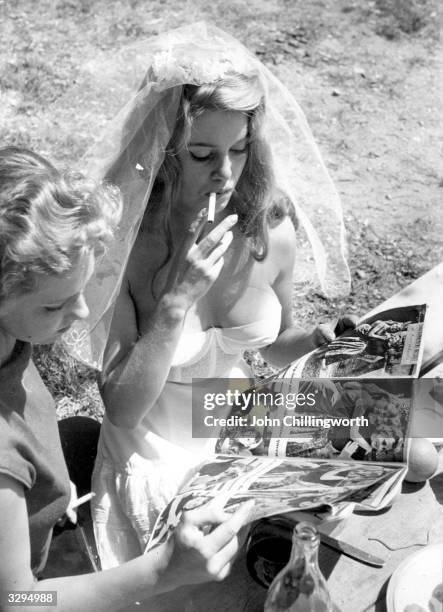 French actress and sex symbol Brigitte Bardot, dressed in a corset and bridal veil, smokes a cigarette while she pages through a photospread of...