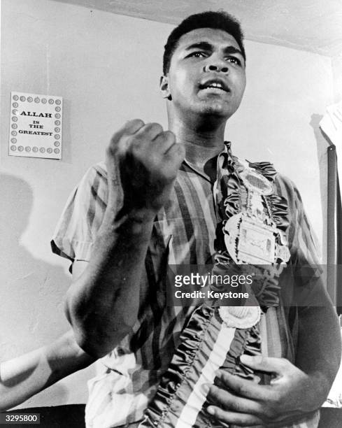 Cassius Clay posing with his belt in front of a sign 'Allah is the Greatest', in his apartment in Miami before his title fight with Sonny Liston for...