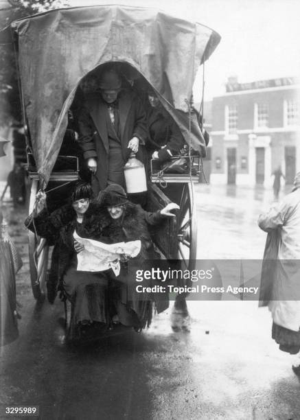 Racegoers travelling to Epsom Downs for the Derby in the back of a horse-drawn wagon: two women study the form.