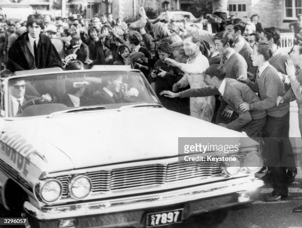 Workmen and schoolchildren mob the car carrying British pop sensation The Beatles from Adelaide airport during their Australian tour.
