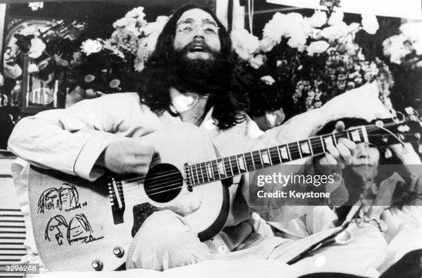 British singer-songwriter John Lennon of Beatles fame sings a song, while his wife Yoko Ono lies in bed beside him. The couple are staying in bed in...