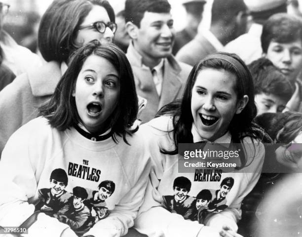 Two excited girls in Beatles sweatshirts, amongst a crowd of fans in New York, welcoming the group as they arrive at the airport.