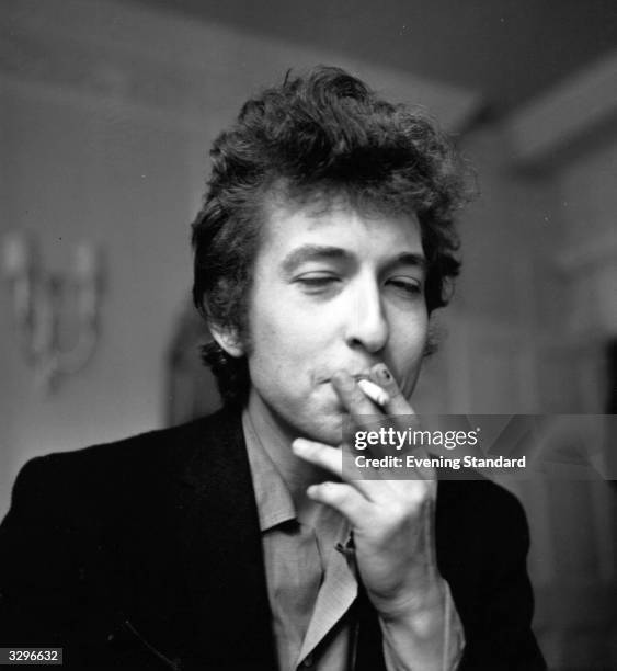 American electric folk hero Bob Dylan smoking a cigarette during a press interview.