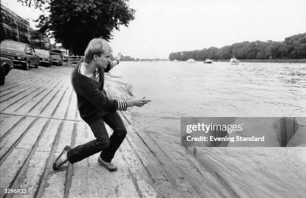 Sting, lead singer and bass player with the pop group The Police, relaxes by skimming stones by the riverbank at Putney, south west London.