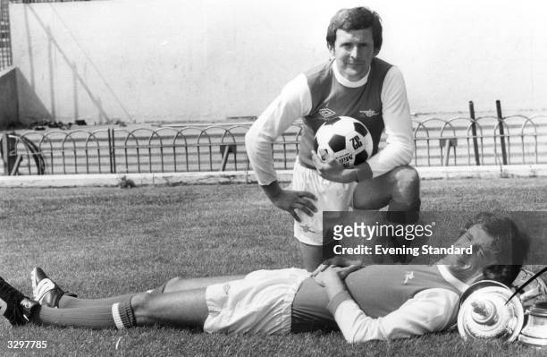 Arsenal Footballers John Hollins and David O'Leary at Highbury. O'Leary appears to be using the FA Cup as a headrest.