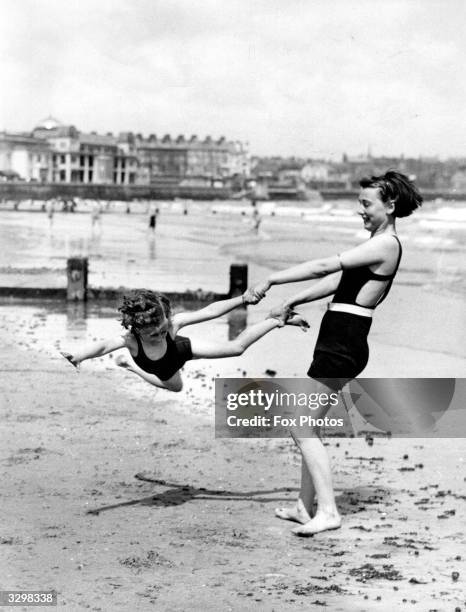 Woman swings a child on the beach at Bridlington, Humberside, during Whitsun holiday.