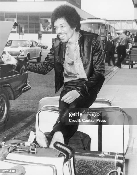 Innovative rock guitarist Jimi Hendrix jokingly thumbs for a lift while waiting with his baggage at Heathrow Airport, London.