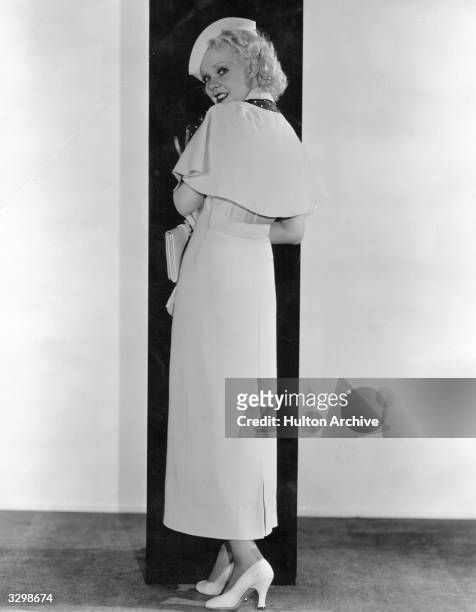 Alice Faye wearing a frock with detachable cape made in heavy white crepe and relieved with navy polka-dotted taffeta. Other accessories include a...