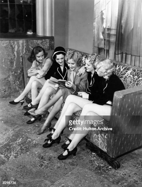 Mae Clarke sits on a couch with four other young girls, giggling and laughing over a book in a scene from the gangster film 'Night World'. Title:...