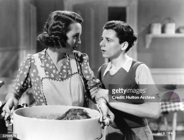 Actress Mary Astor talks with Freddie Bartholomew over a large cooking pot in a scene from the film 'Listen, Darling', in which three children try to...