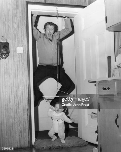 The Scottish star of the Black and White Ministrel Show, Don Arrol, at his home in Surrey, hanging from the door frame while his baby daughter, Fiona...