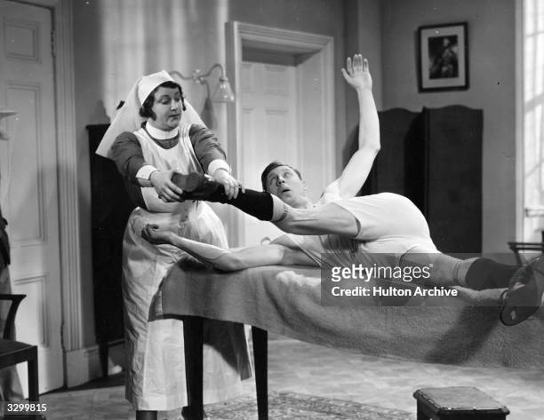 George Formby , the British comedian and ukelele player is wrestling with a nurse, who is trying to remove his clothes in a scene from 'Keep Your...