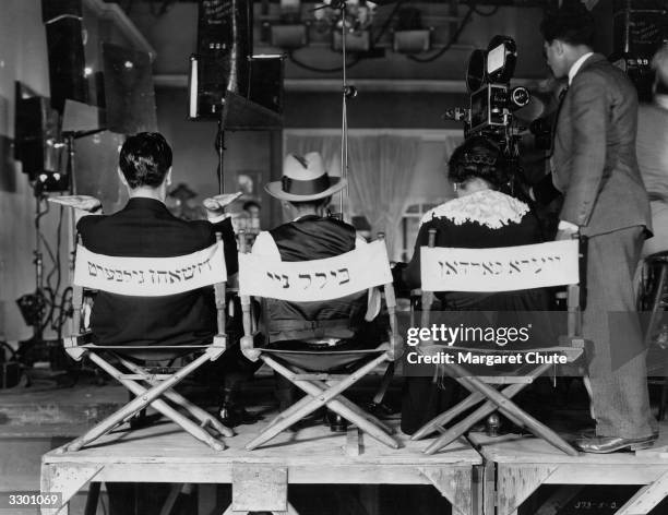 Actors Vera Gordon and John Gilbert, and director William Nigh sitting in chairs which have been inscribed with their names in Yiddish, at the...