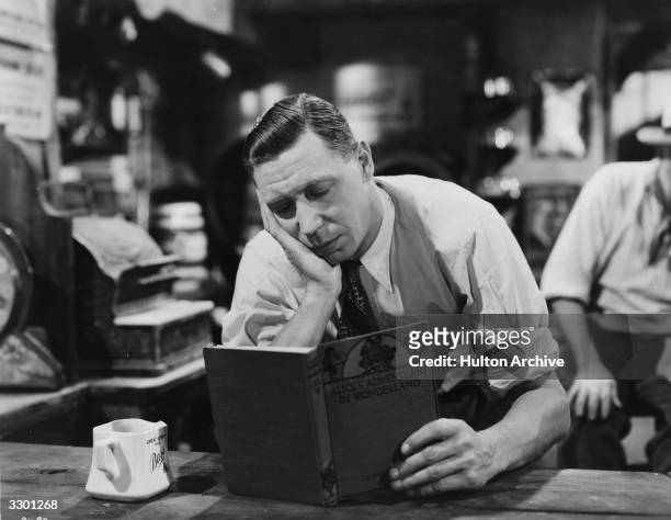 British comedian George Formby buries himself in a book in the Columbia comedy 'George In Civvy Street', directed by Marcel Varnel.