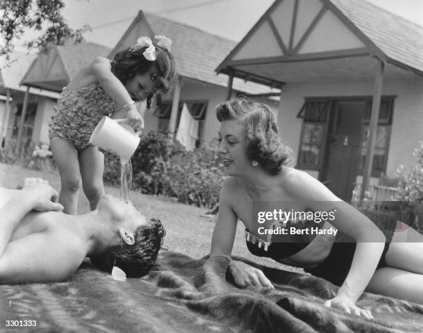 Young girl pours water over her sleeping father at a Butlin's holiday camp in Filey. Original Publication: Picture Post - 6589 - Picture Post Visits...