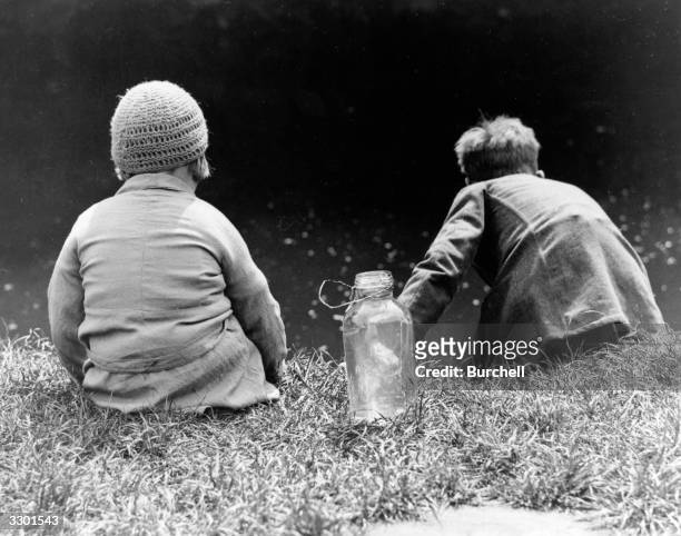Two children sitting on a river bank fishing for tiddlers at Snuff MIlls, Bristol.