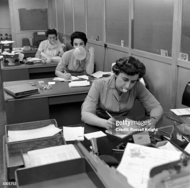 Secretaries in the office of Topps Chewing Gum Factory in Brooklyn, New York, blowing bubbles as they work. Right to left, they are Mildred Muller,...