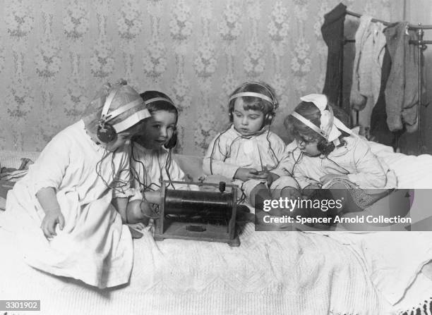 Group of young children sitting on a bed listening to the radio on headphones.